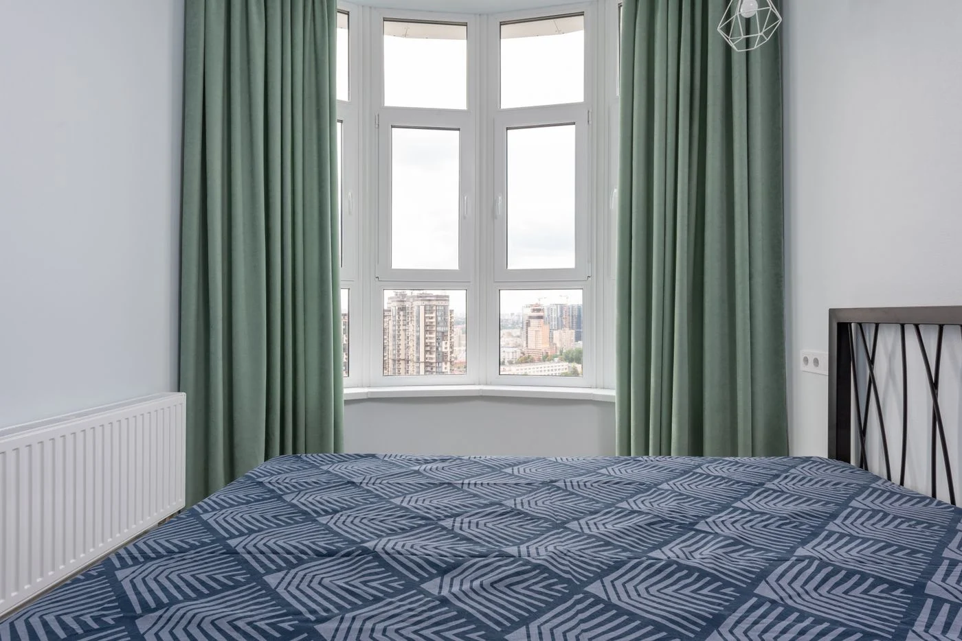 Doppelbett mit blauer Tagesdecke neben einem Fenster